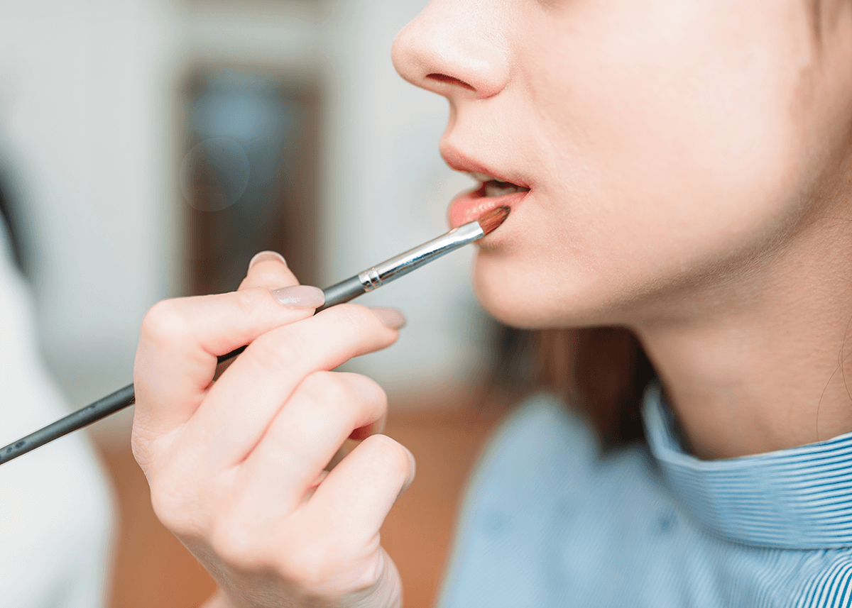 Makeup Artist Hand Applying Gloss on Woman's Lips
