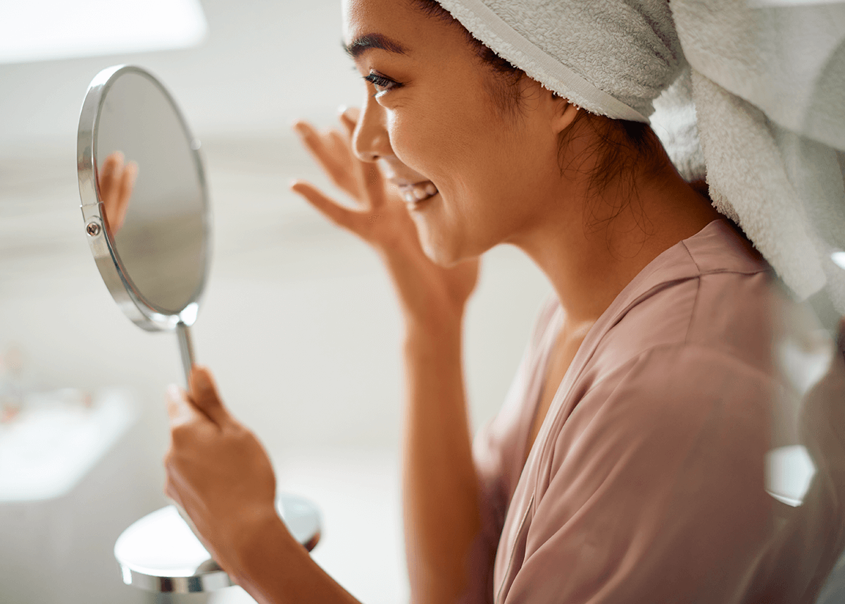 Woman Applying Moisturizer to Face in Hand Mirror