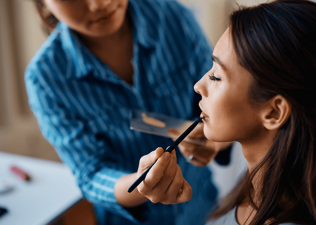 Makeup artist applying lipstick with brush on woman's lips
