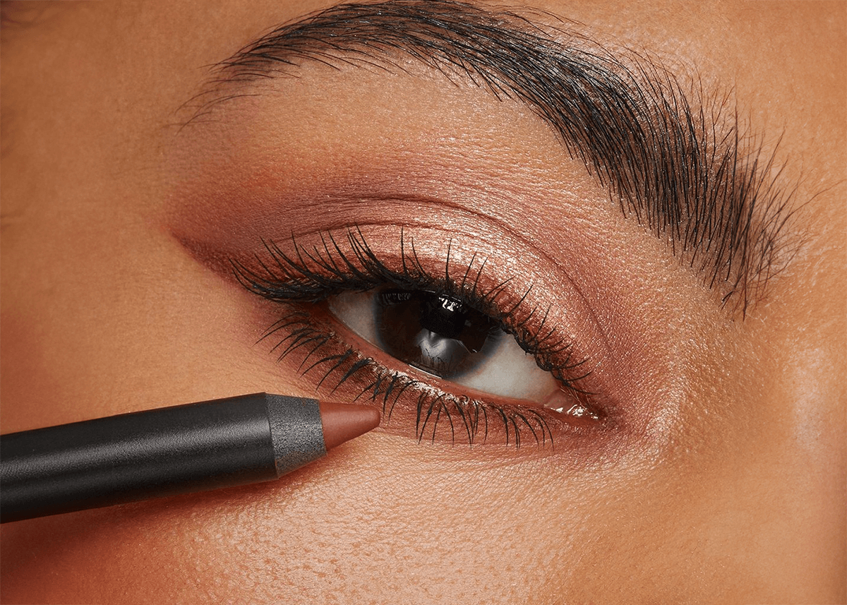 A woman applying pencil eyeliner