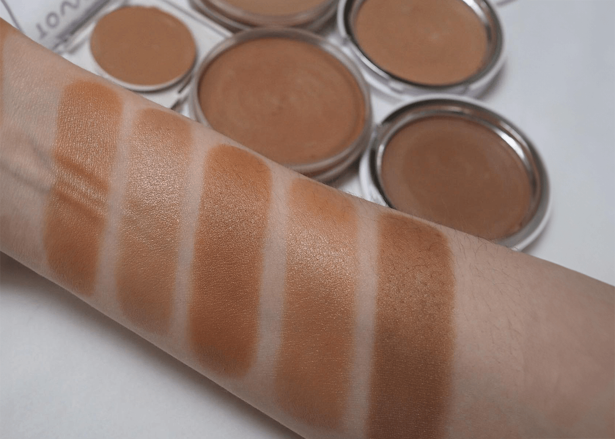 A woman with different skin tones swatching different shades of bronzer on her arm